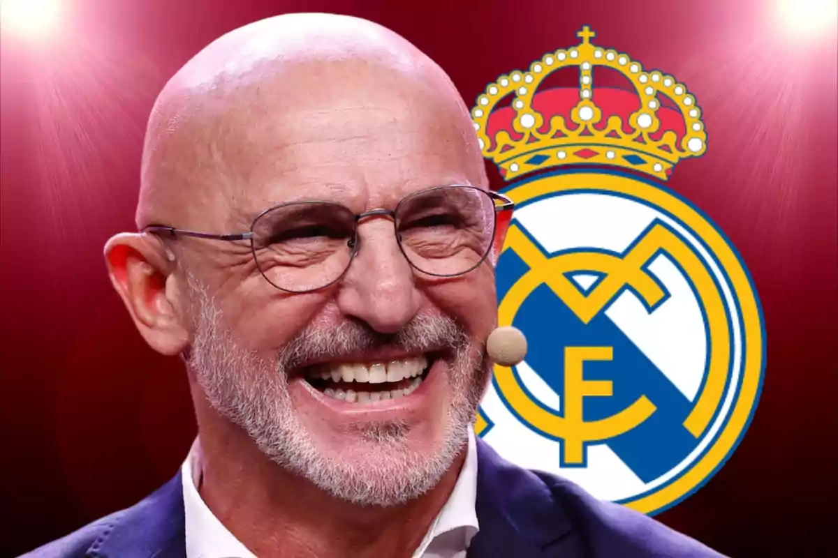 Bald man with glasses and a microphone smiles in front of the Real Madrid crest against a red background