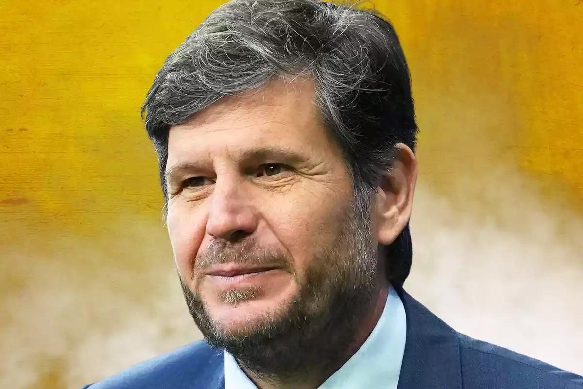 Gray-haired man with a short beard wearing a blue jacket against a blurred yellow background