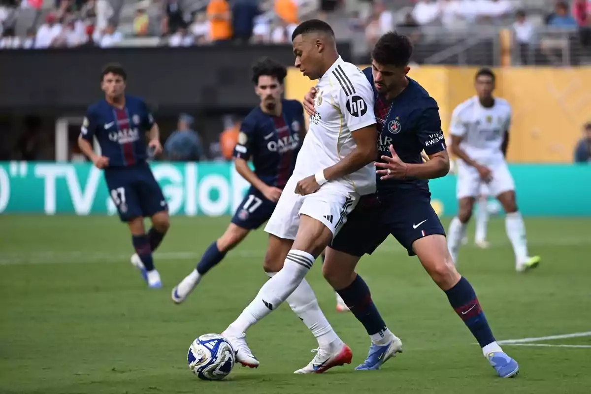 Dos futbolistes disputen la pilota durant un partit entre el Reial Madrid i el PSG mentre altres jugadors observen la jugada al fons del camp. Dos futbolistes disputen la pilota durant un partit entre el Reial Madrid i el PSG mentre altres jugadors observen la jugada al fons del camp.