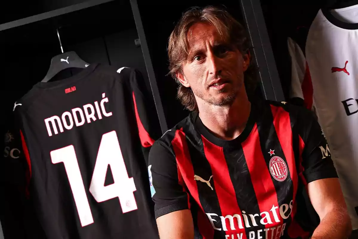A player wearing the AC Milan uniform is sitting in a locker room next to a jersey hanging with the name Modric and the number 14. A player wearing the AC Milan uniform is sitting in a locker room next to a jersey hanging with the name Modric and the number 14.