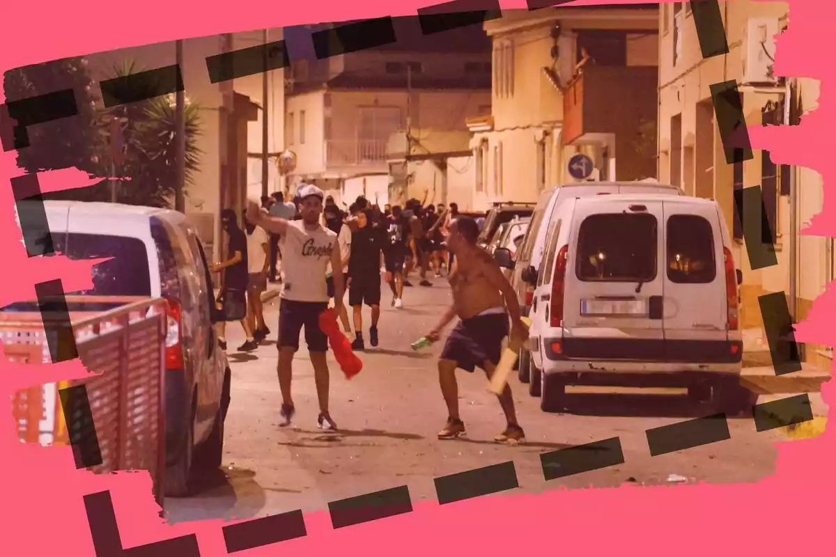 Grup de persones en un carrer durant la nit, algunes semblen estar discutint o barallant-se, envoltades de cotxes aparcats i amb un marc decoratiu rosa.