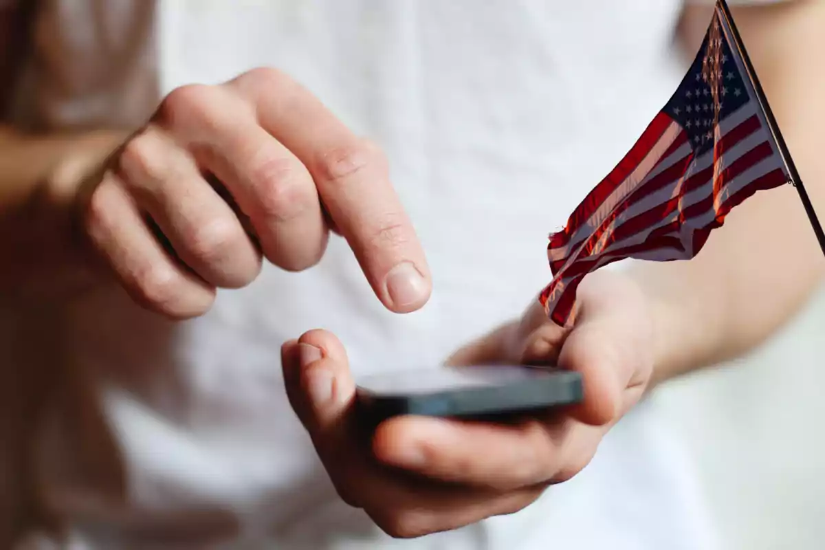 Person using a mobile phone with a small United States flag in their hand Person using a mobile phone with a small United States flag in their hand