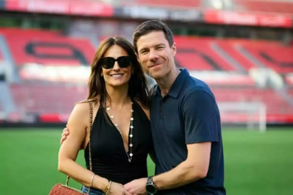 Una pareja sonriente, formada por Xabi Alonso y Nagore Aranburu, posando en un estadio de fútbol con gradas rojas de fondo. Una pareja sonriente, formada por Xabi Alonso y Nagore Aranburu, posando en un estadio de fútbol con gradas rojas de fondo.