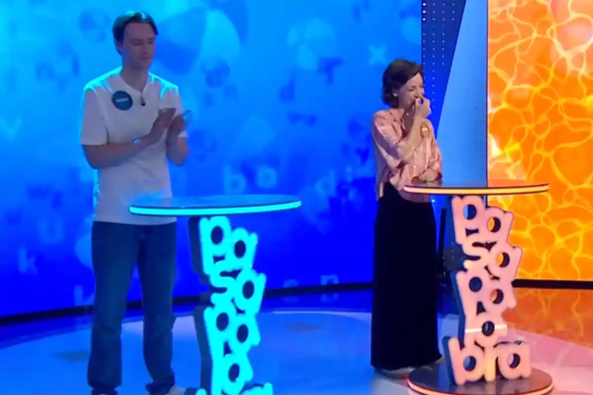 Manu i Rosa participen en un programa de televisió de preguntes i respostes, l’un aplaudeix mentre l’altra somriu emocionada al costat dels seus faristols il·luminats. Captura de ‘Pasapalabra’ Manu i Rosa participen en un programa de televisió de preguntes i respostes, l’un aplaudeix mentre l’altra somriu emocionada al costat dels seus faristols il·luminats. Captura de ‘Pasapalabra’