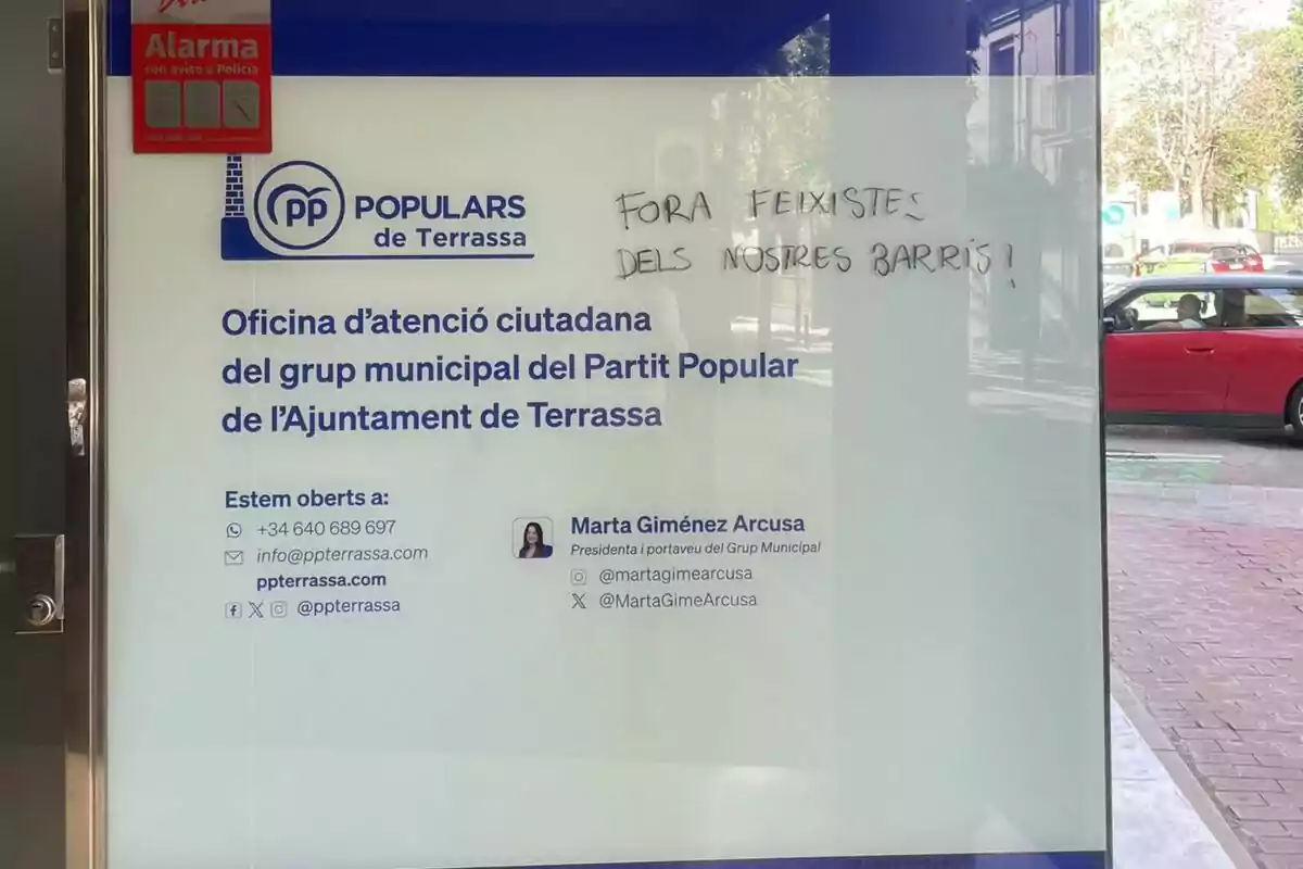 Porta de vidre de l’oficina del Partit Popular de Terrassa amb informació de contacte i un missatge escrit a mà que diu Porta de vidre de l’oficina del Partit Popular de Terrassa amb informació de contacte i un missatge escrit a mà que diu