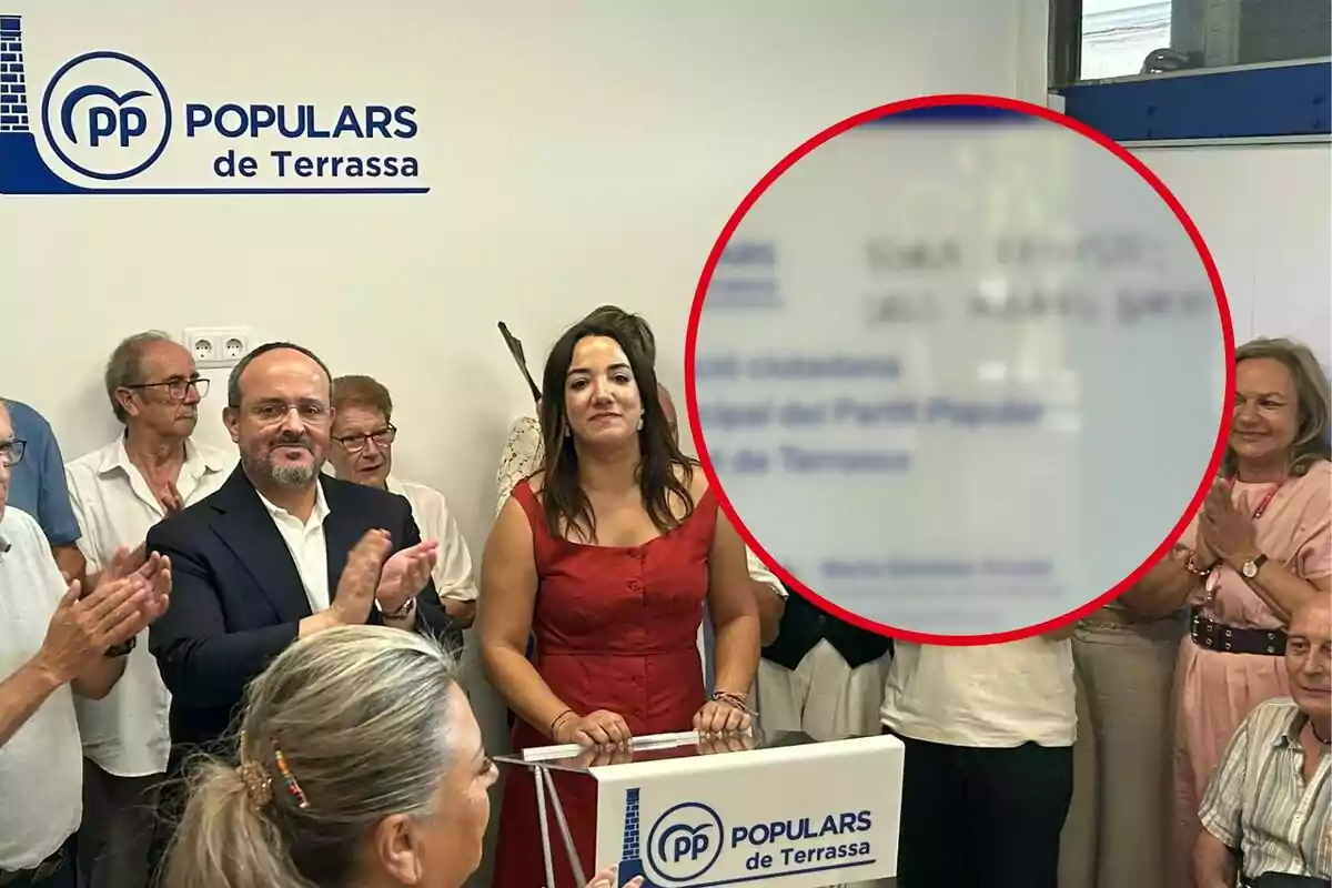 Un grup de persones aplaudeix en un acte del Partit Popular de Terrassa, amb una dona al centre darrere d’un faristol i el logotip del partit a la paret.