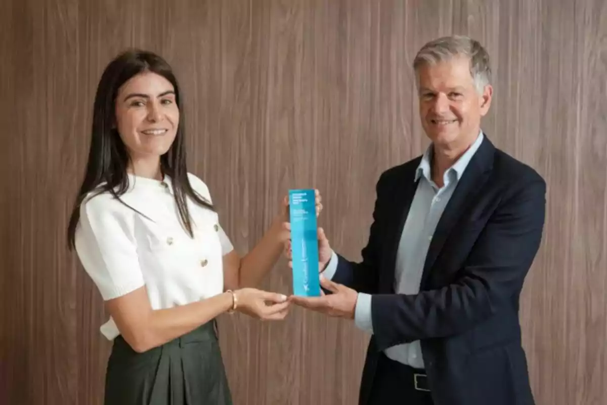 Dues persones somrients sostenen juntes un trofeu blau davant d’una paret de fusta Dues persones somrients sostenen juntes un trofeu blau davant d’una paret de fusta