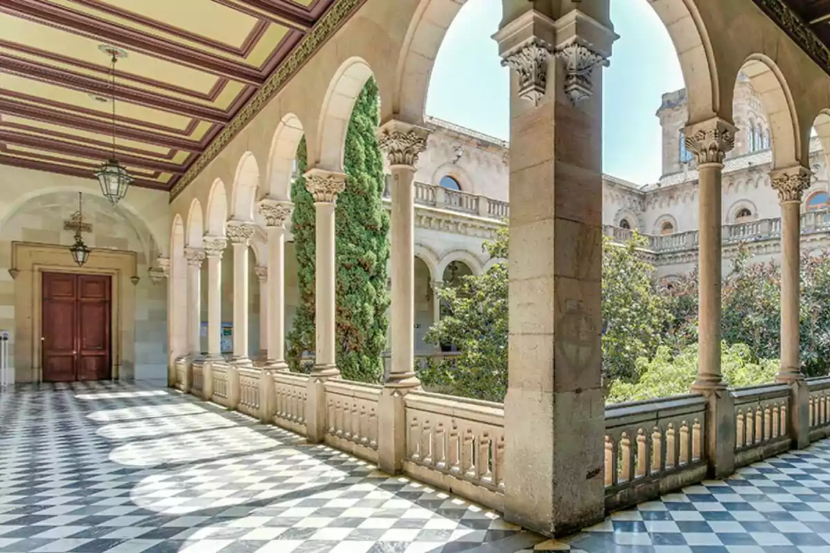 Hallway with stone columns and arches, black and white tiled floor, and a view of a garden with trees Hallway with stone columns and arches, black and white tiled floor, and a view of a garden with trees