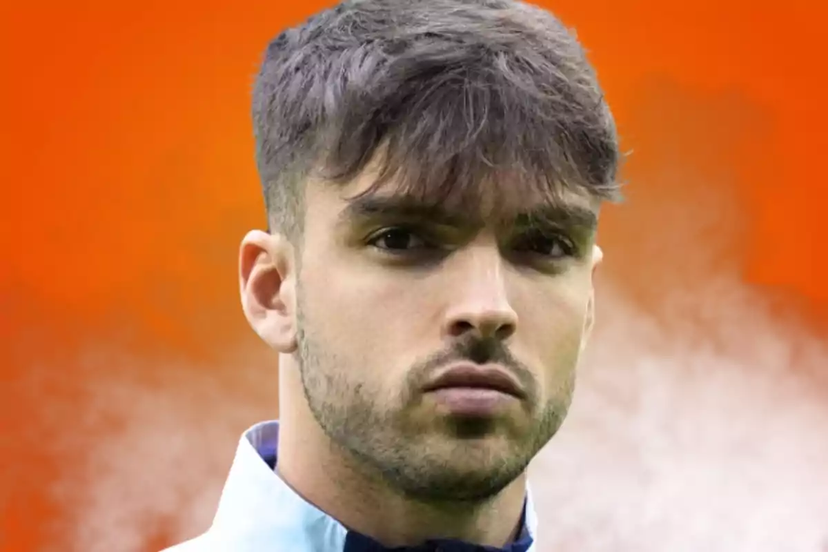 Young man with short hair and a light beard, wearing a serious expression against a blurred orange background