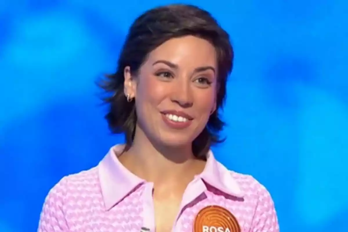 Rosa Rodríguez, concursant de 'Pasapalabra', somriu mentre participa en aquest programa de televisió, porta una camisa rosa amb coll i una insígnia taronja amb el nom Rosa sobre un fons blau. Rosa Rodríguez, concursant de 'Pasapalabra', somriu mentre participa en aquest programa de televisió, porta una camisa rosa amb coll i una insígnia taronja amb el nom Rosa sobre un fons blau.