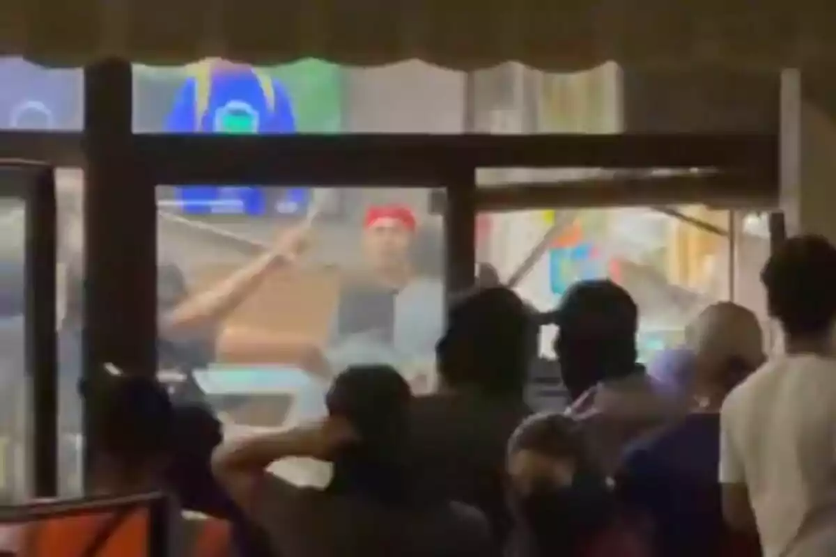 Several people watch a fight inside a venue while a man with a red cap is at the center of the scene. Several people watch a fight inside a venue while a man with a red cap is at the center of the scene.
