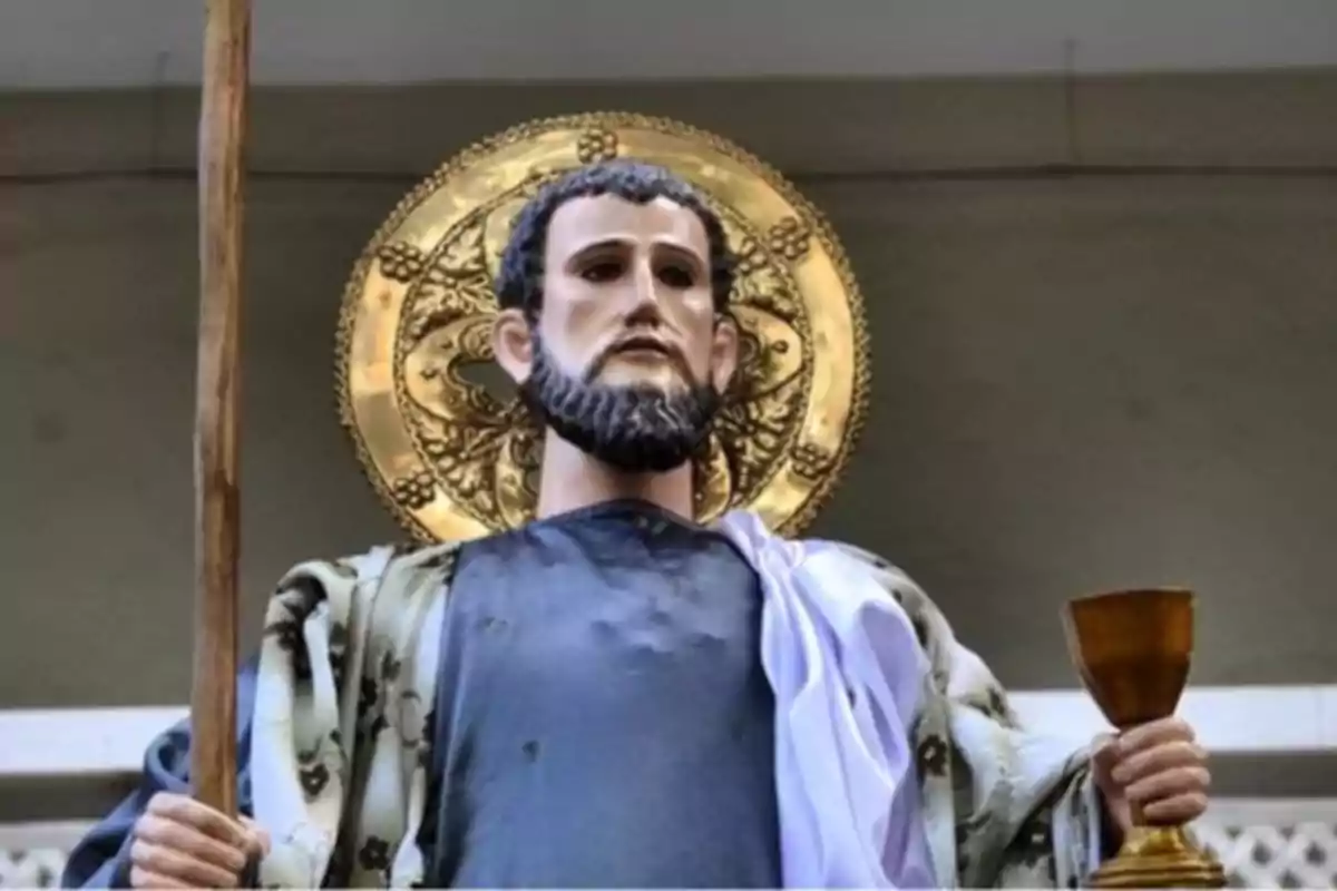 Escultura religiosa d’un home amb barba que sosté un bastó en una mà i una copa daurada a l’altra, amb un halo daurat darrere del cap. Escultura religiosa d’un home amb barba que sosté un bastó en una mà i una copa daurada a l’altra, amb un halo daurat darrere del cap.