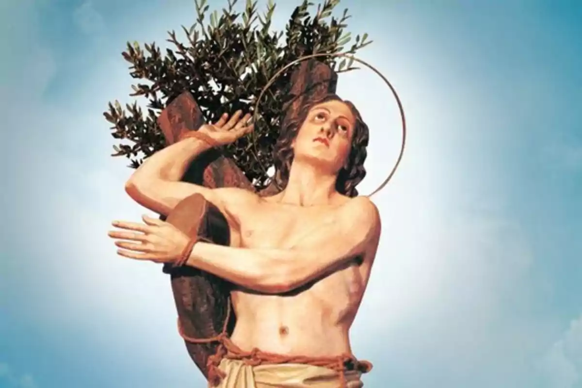 Escultura religiosa de un hombre atado a un tronco con una aureola dorada y ramas de olivo al fondo sobre un cielo azul Escultura religiosa de un hombre atado a un tronco con una aureola dorada y ramas de olivo al fondo sobre un cielo azul
