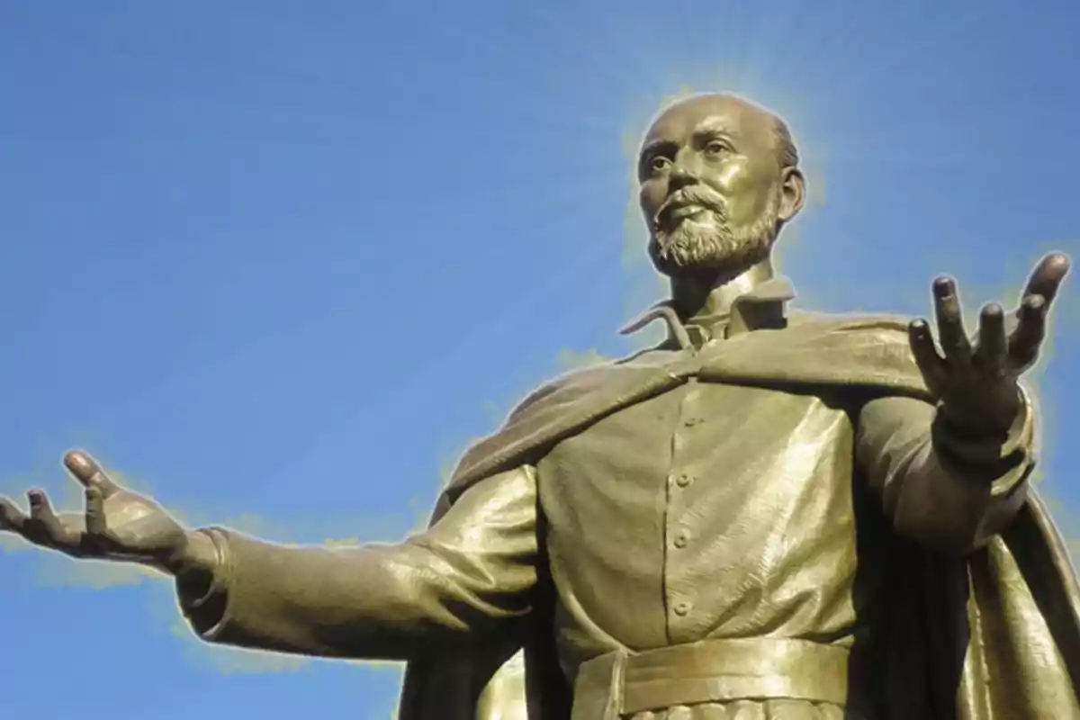 Estàtua d’un home amb barba i els braços estesos cap als costats, amb una resplendor al voltant del cap i un cel blau de fons Estàtua d’un home amb barba i els braços estesos cap als costats, amb una resplendor al voltant del cap i un cel blau de fons