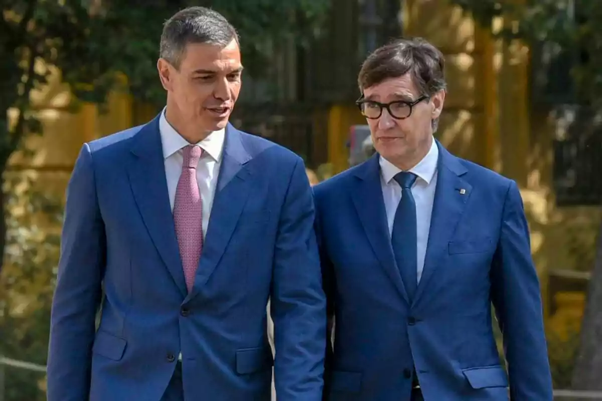 Dos homes vestits amb vestit blau caminen junts a l’aire lliure mentre conversen