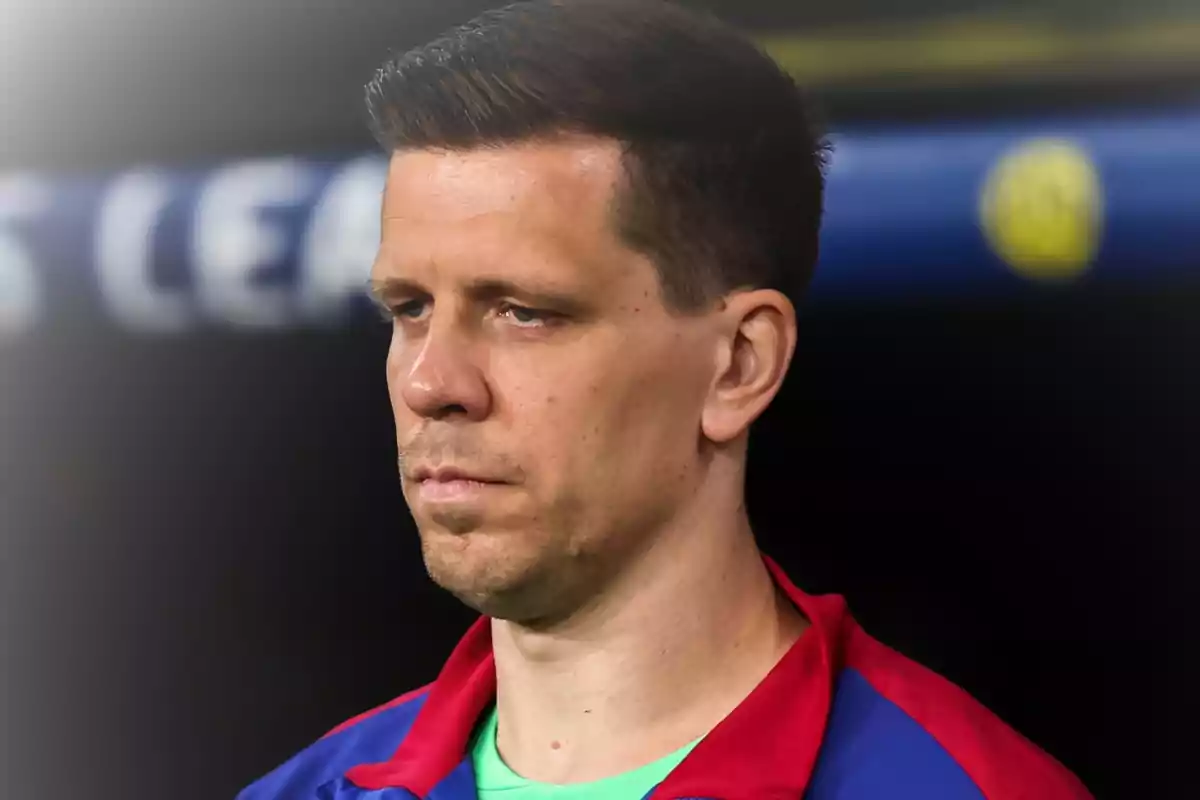Short-haired man with a serious expression wearing a blue and red sports jacket in a sports setting
