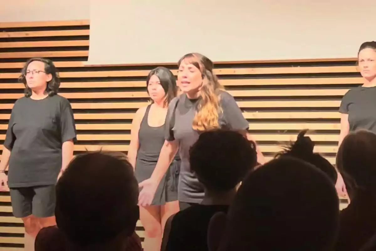 Quatre dones vestides de negre actuen sobre un escenari de fusta davant d’un públic. Quatre dones vestides de negre actuen sobre un escenari de fusta davant d’un públic.