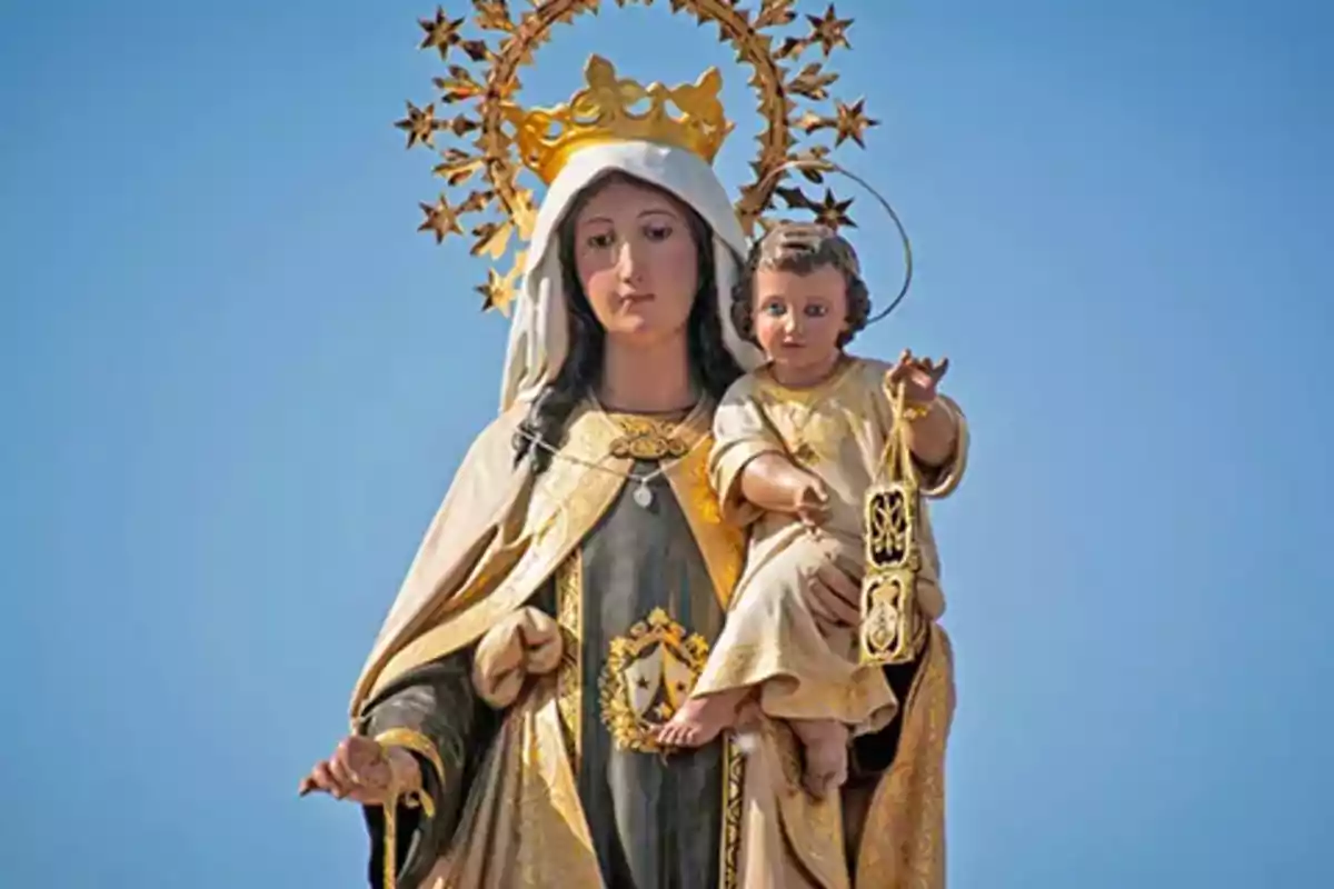 Escultura religiosa d’una verge amb corona daurada sostenint el nen Jesús sota un cel blau