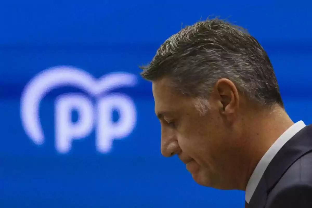 Hombre de perfil con expresión seria frente a un fondo azul con el logotipo del Partido Popular desenfocado Hombre de perfil con expresión seria frente a un fondo azul con el logotipo del Partido Popular desenfocado
