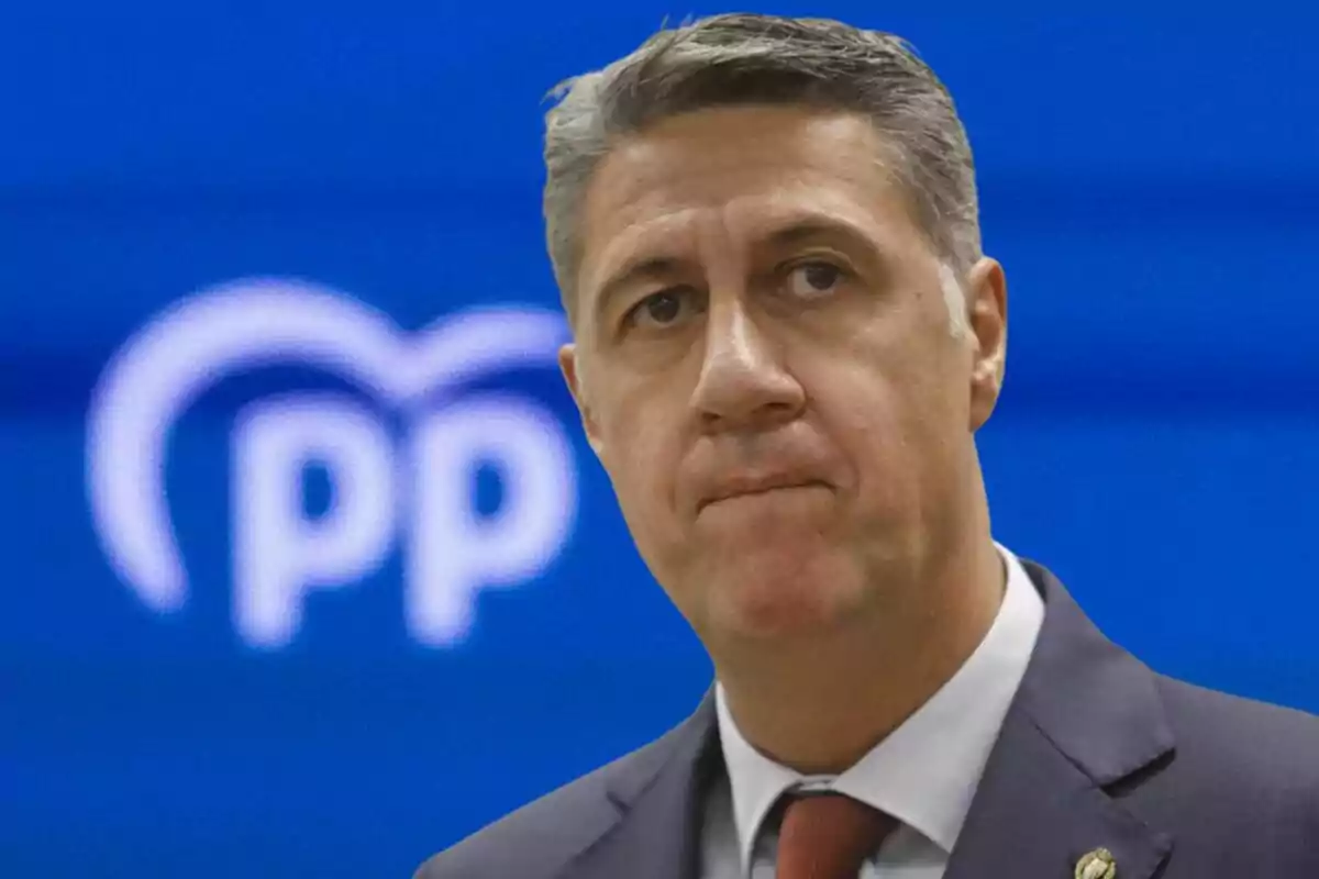 Man in a suit with a serious expression in front of a blue background with the blurred People's Party logo