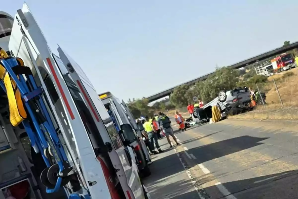 Varias ambulancias y personal de emergencia atienden un accidente de tráfico con un coche volcado en una carretera rural. Varias ambulancias y personal de emergencia atienden un accidente de tráfico con un coche volcado en una carretera rural.