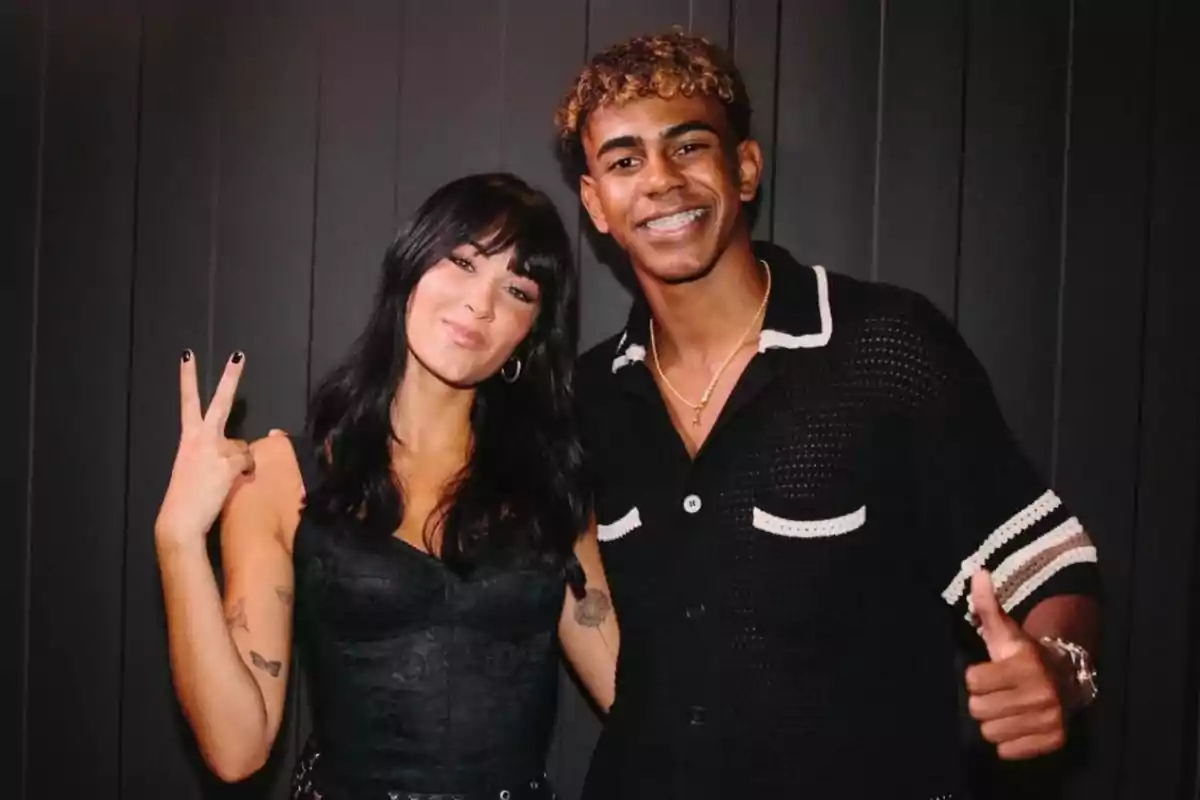Aitana Ocaña i Lamine Yamal posen somrients davant d’una paret fosca, la dona fa el signe de la pau amb la mà i l’home mostra un polze amunt. Aitana Ocaña i Lamine Yamal posen somrients davant d’una paret fosca, la dona fa el signe de la pau amb la mà i l’home mostra un polze amunt.