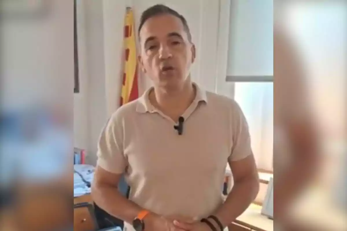 Hombre de pie en una oficina con una bandera detrás y usando un micrófono de solapa