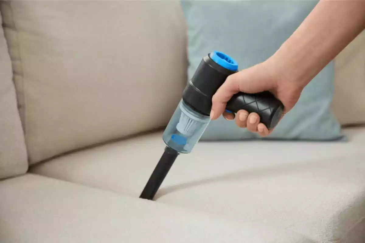 Persona usando una aspiradora de mano para limpiar un sofá beige Persona usando una aspiradora de mano para limpiar un sofá beige