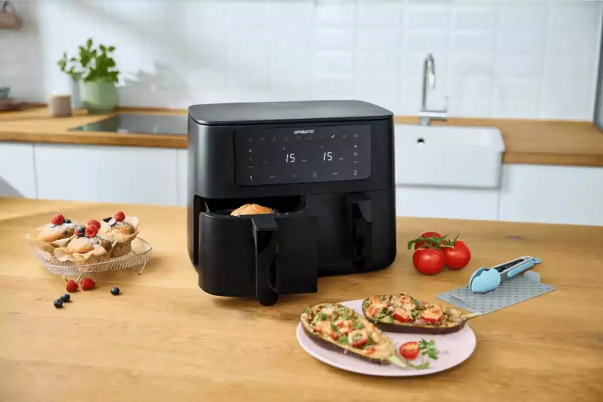 Freidora de aire negra de doble compartimento en una cocina moderna con muffins, berenjenas rellenas y tomates sobre la mesa Freidora de aire negra de doble compartimento en una cocina moderna con muffins, berenjenas rellenas y tomates sobre la mesa