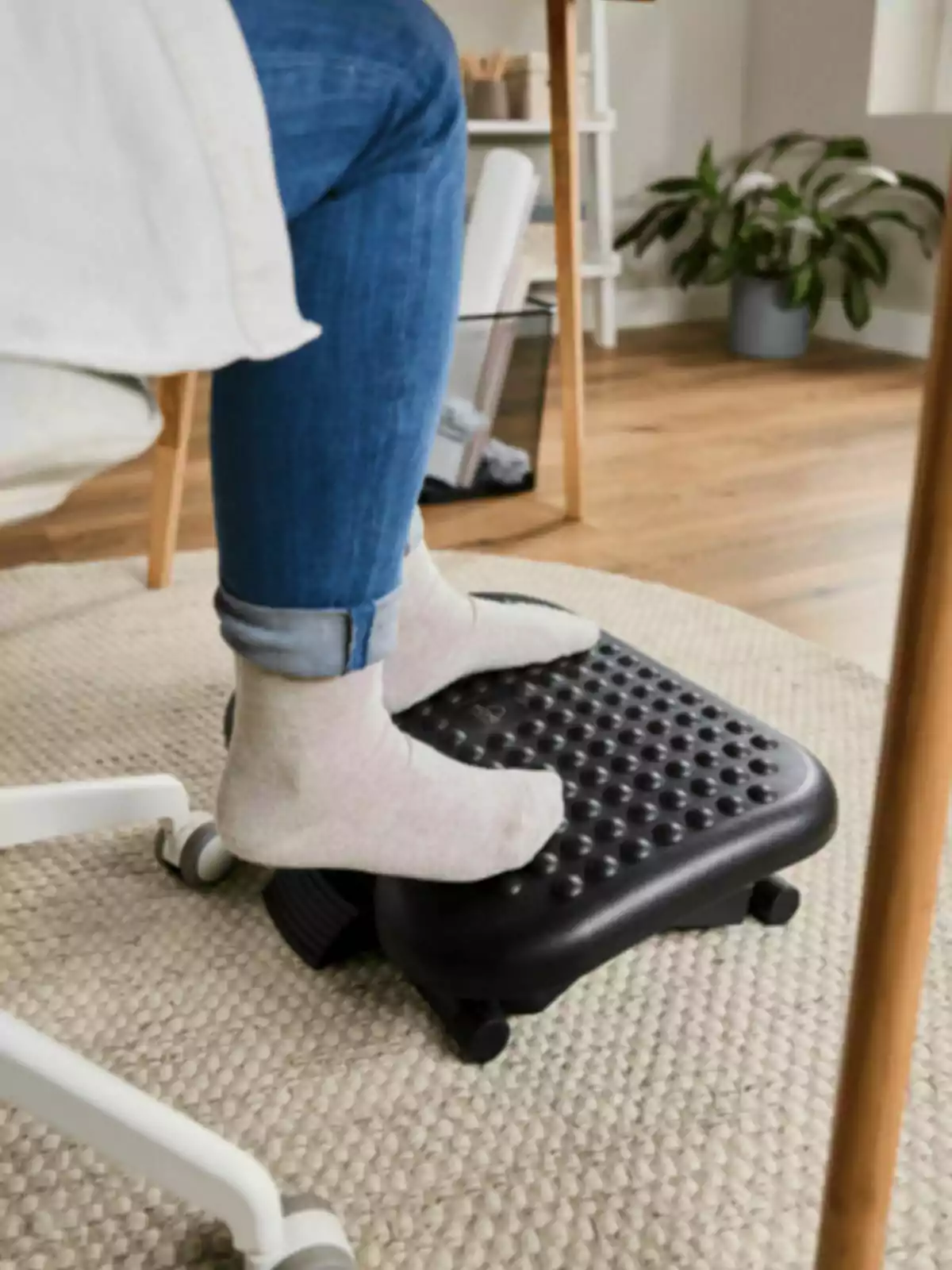 Persona amb mitjons clars utilitzant un reposapeus ergonòmic negre en una oficina domèstica amb terra de fusta i catifa beix. Persona amb mitjons clars utilitzant un reposapeus ergonòmic negre en una oficina domèstica amb terra de fusta i catifa beix.