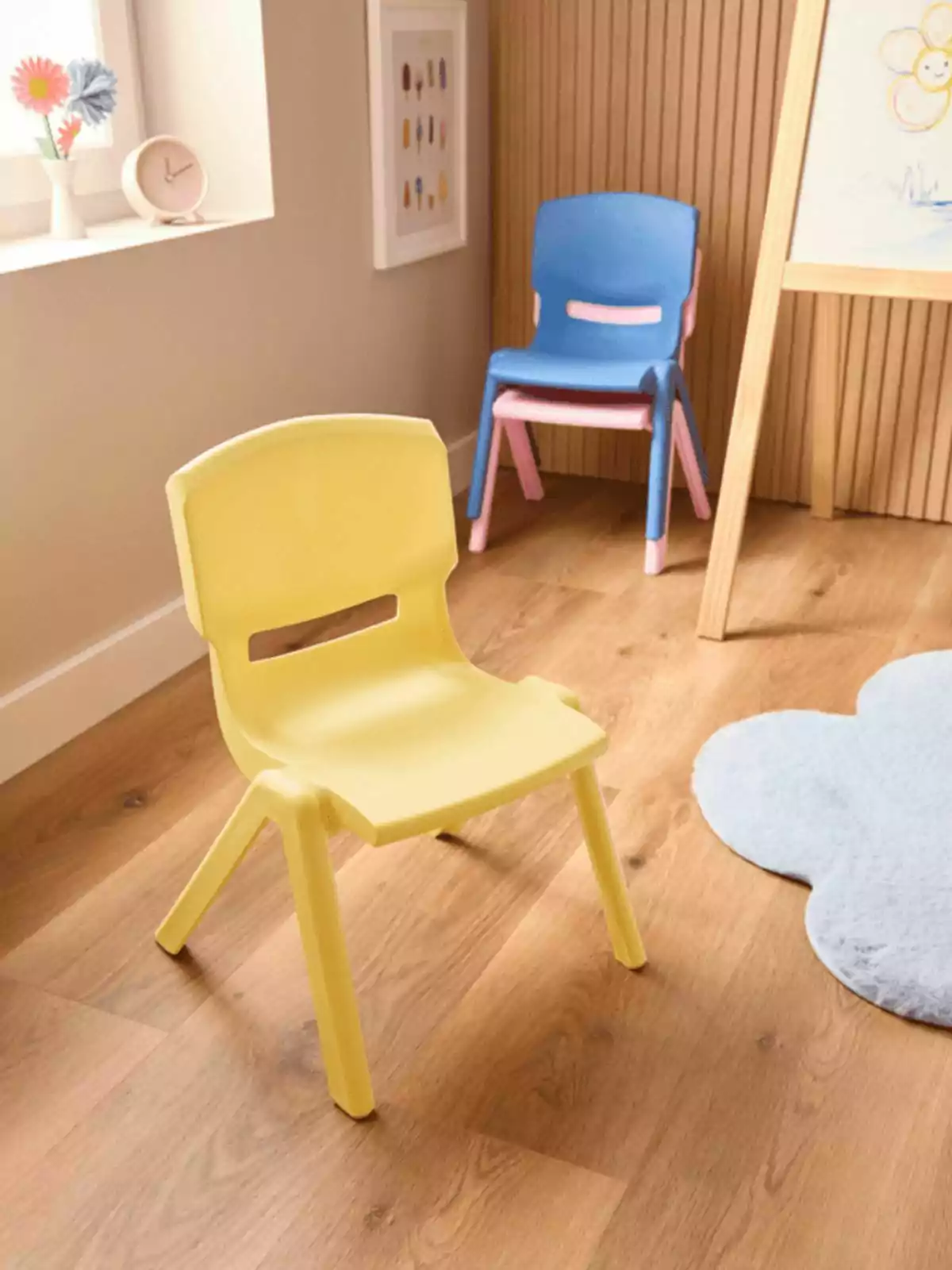Cadira infantil groga de plàstic en primer pla amb dues cadires apilades al fons en una habitació infantil amb terra de fusta Cadira infantil groga de plàstic en primer pla amb dues cadires apilades al fons en una habitació infantil amb terra de fusta
