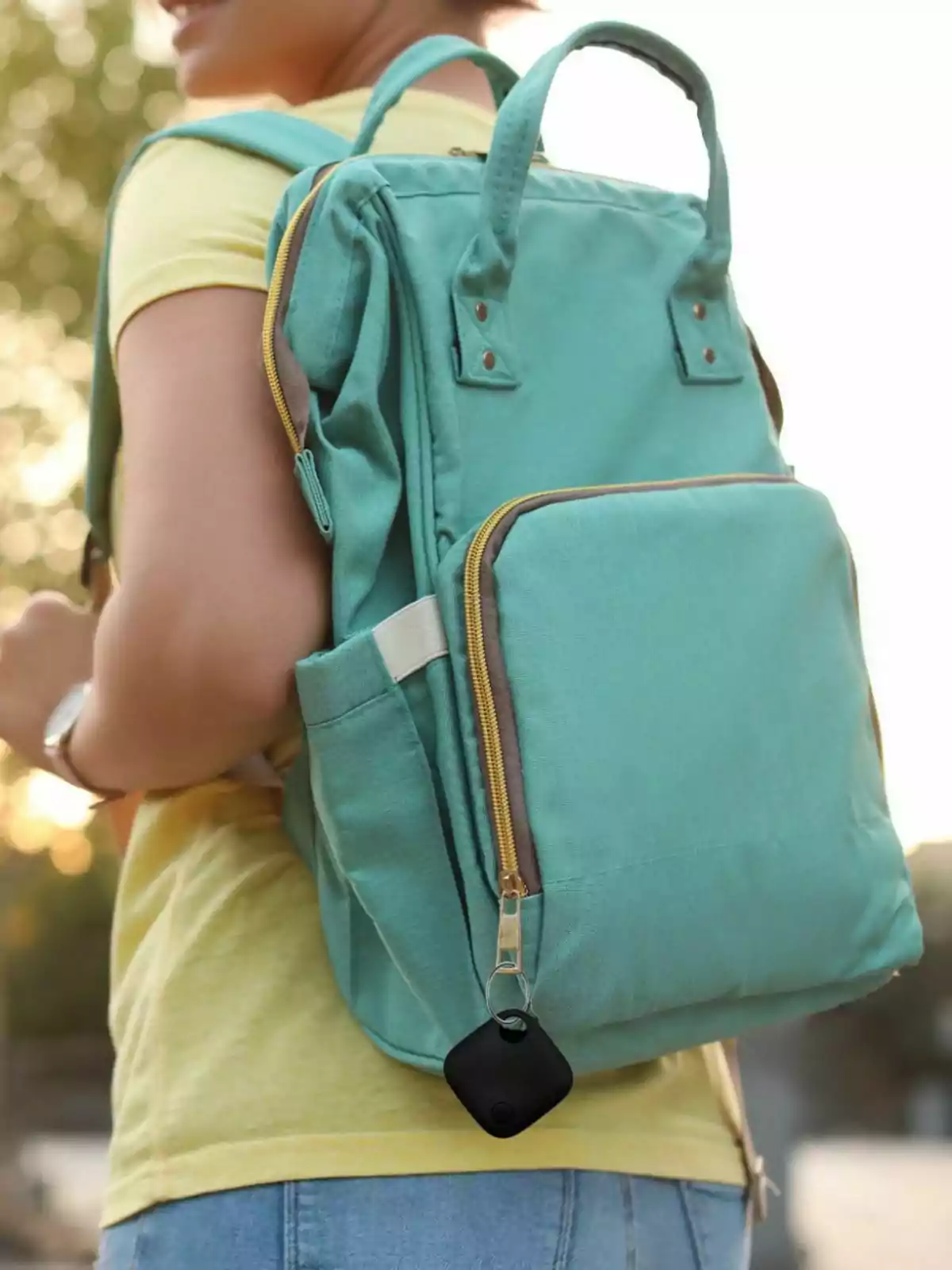 Persona de espaldas usando una mochila verde menta con un llavero localizador negro colgado del cierre frontal Persona de espaldas usando una mochila verde menta con un llavero localizador negro colgado del cierre frontal