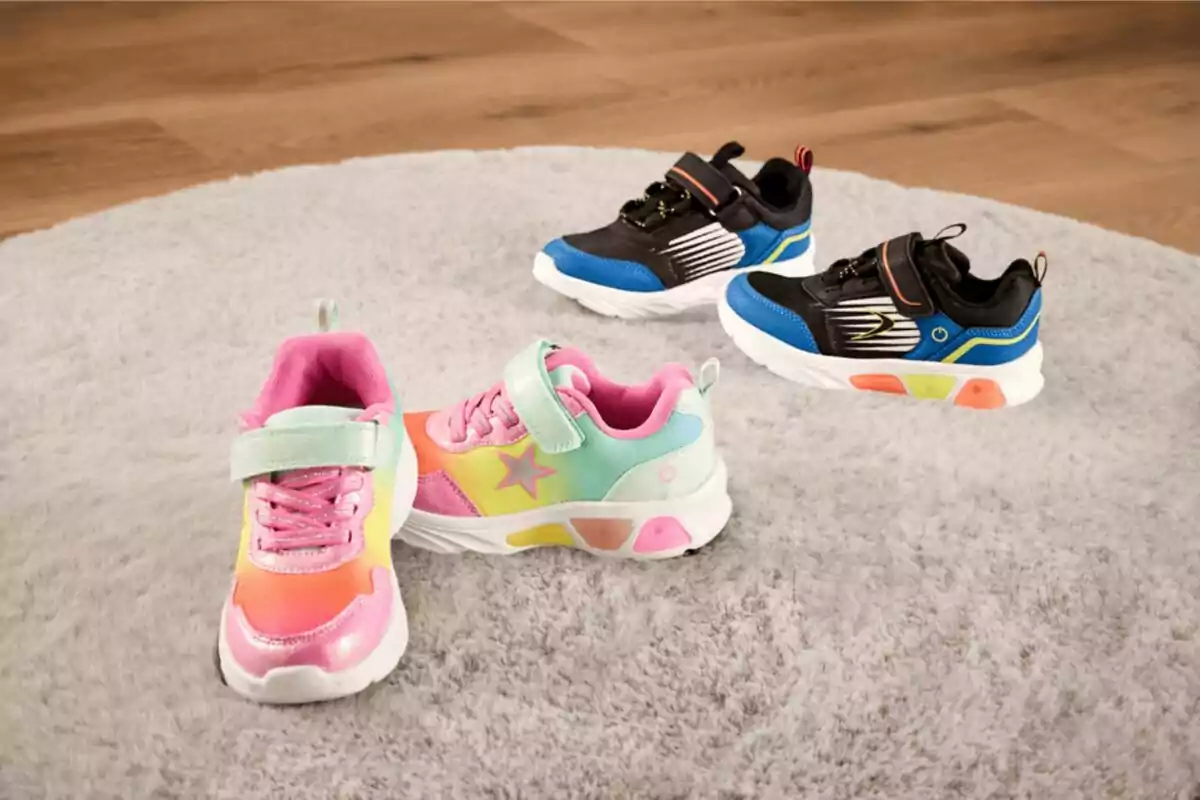 Cuatro tenis infantiles de colores vivos están sobre una alfombra gris, dos pares en tonos rosa y azul con detalles llamativos Cuatro tenis infantiles de colores vivos están sobre una alfombra gris, dos pares en tonos rosa y azul con detalles llamativos