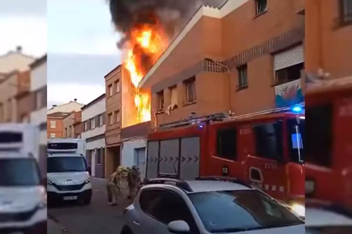 Incendi en un edifici de diversos pisos amb bombers i un camió de bombers treballant al carrer