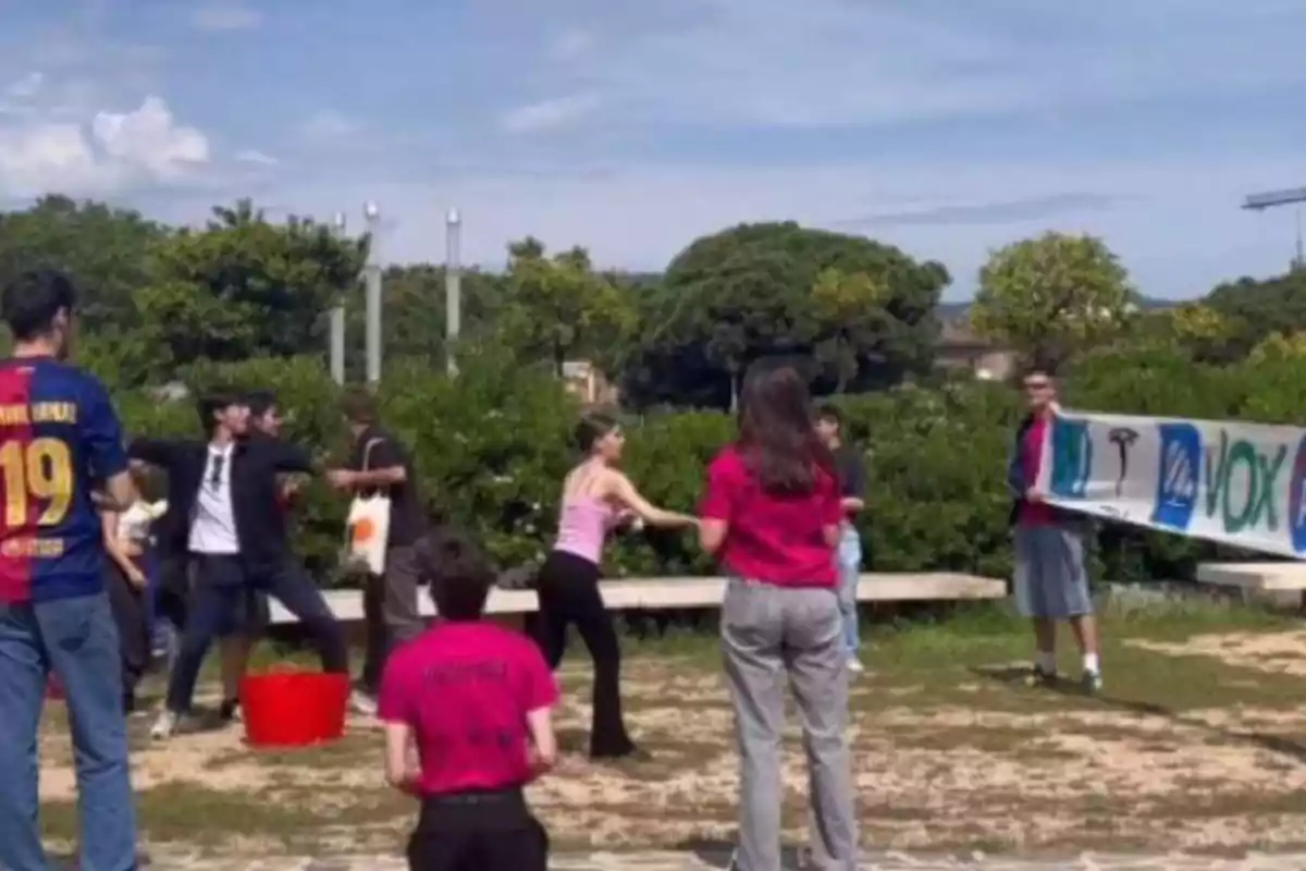 Un grupo de jóvenes participa en una manifestación al aire libre donde algunos sostienen una pancarta y otros parecen estar discutiendo o forcejeando en un parque