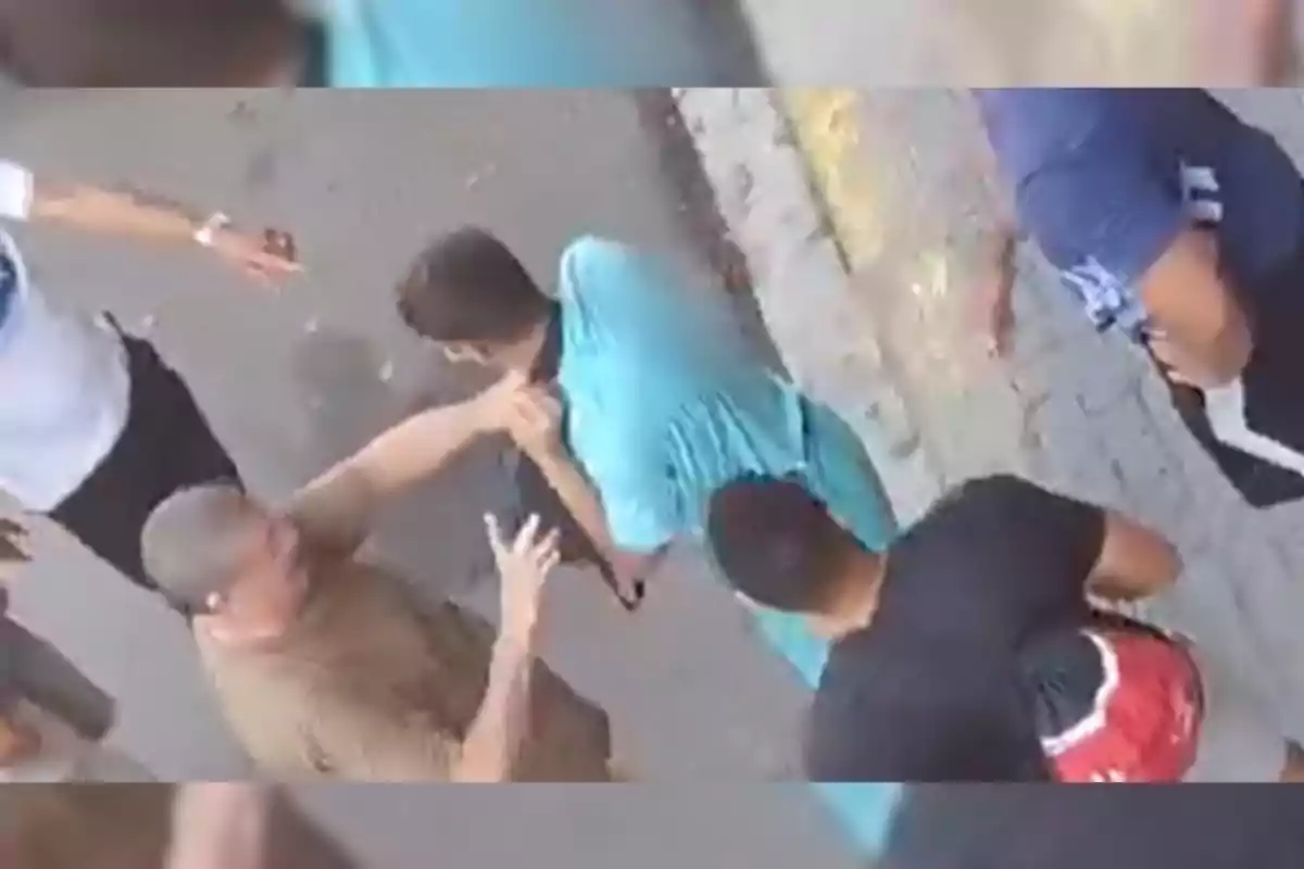 Varias personas rodean a un joven al que uno de ellos sujeta por la camiseta en una calle junto a la banqueta