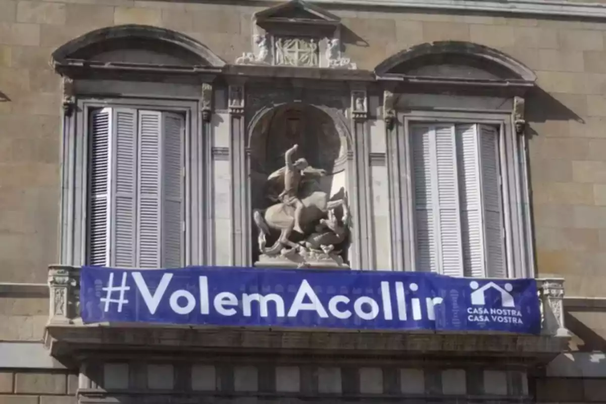 Fachada de edificio con una estatua ecuestre y una pancarta azul que dice #VolemAcollir