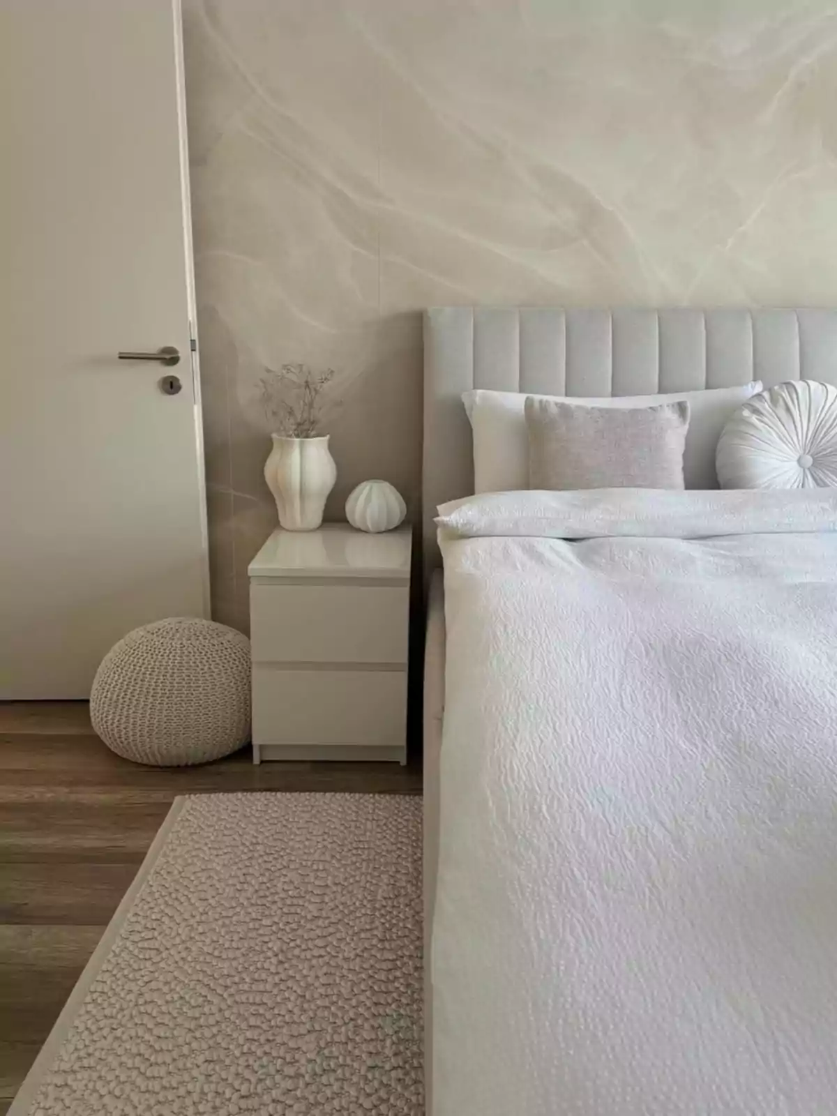 Habitación minimalista con cama de cabecera gris, ropa de cama blanca, cojines decorativos, buró blanco con jarrones y alfombra tejida en tonos neutros Habitación minimalista con cama de cabecera gris, ropa de cama blanca, cojines decorativos, buró blanco con jarrones y alfombra tejida en tonos neutros