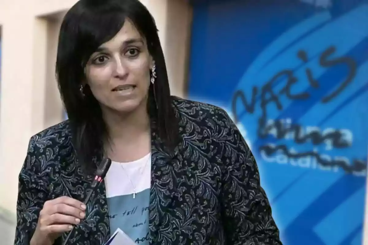 Mujer de cabello oscuro hablando frente a un micrófono con fondo azul donde hay un grafiti que dice "nazis"
