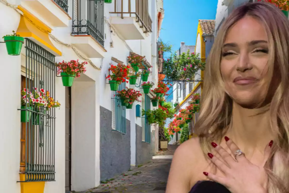 Dona rossa somrient amb la mà al pit davant d’un carrer estret decorat amb testos de flors a les parets blanques Dona rossa somrient amb la mà al pit davant d’un carrer estret decorat amb testos de flors a les parets blanques