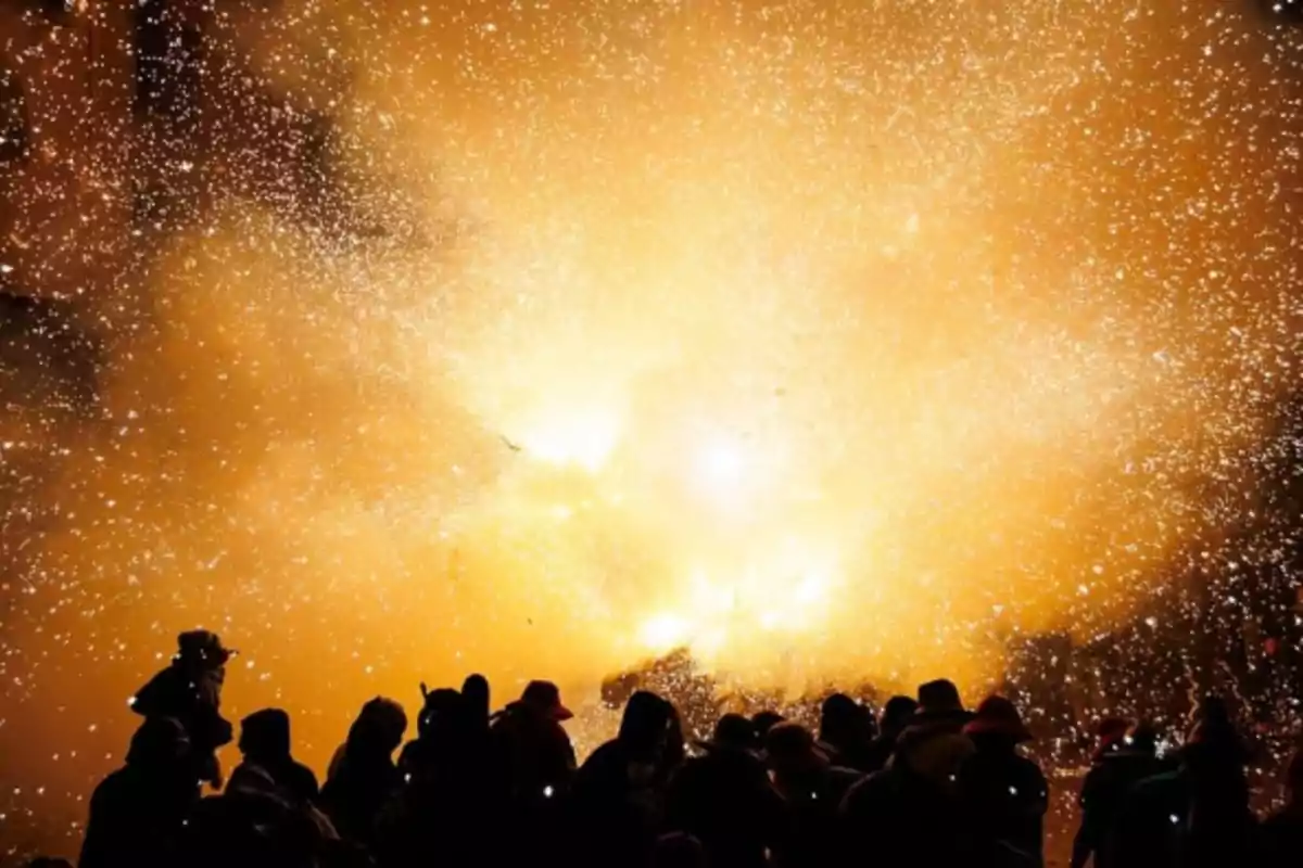 Personas observan un espectáculo de fuegos artificiales con chispas y destellos naranjas iluminando el cielo nocturno Personas observan un espectáculo de fuegos artificiales con chispas y destellos naranjas iluminando el cielo nocturno