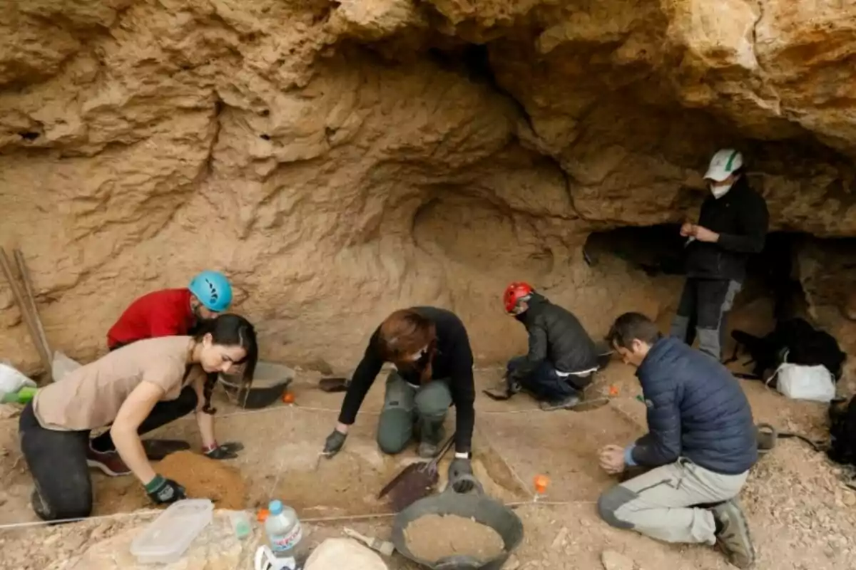 Un grupo de personas realiza una excavación arqueológica en el interior de una cueva, utilizando herramientas y cubetas para recolectar tierra y objetos. Un grupo de personas realiza una excavación arqueológica en el interior de una cueva, utilizando herramientas y cubetas para recolectar tierra y objetos.