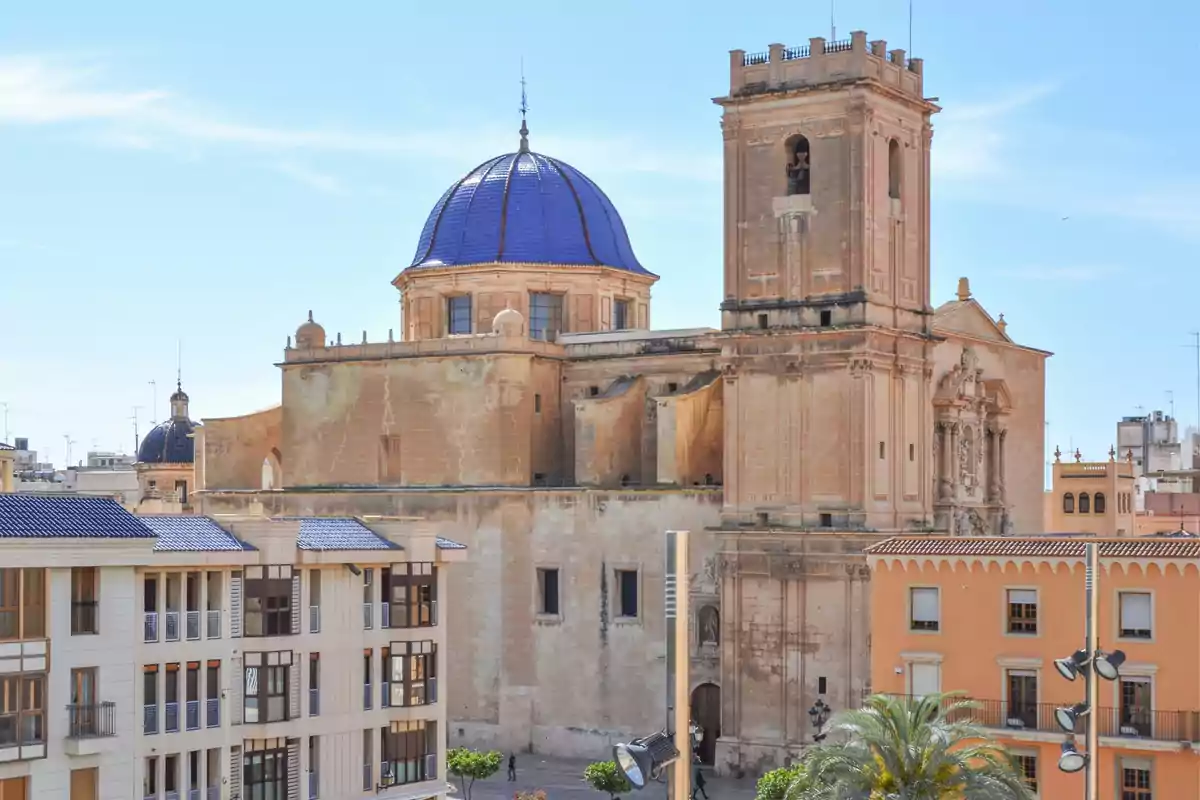 Catedral de piedra con cúpula azul y torre campanario rodeada de edificios en una ciudad bajo un cielo despejado Catedral de piedra con cúpula azul y torre campanario rodeada de edificios en una ciudad bajo un cielo despejado