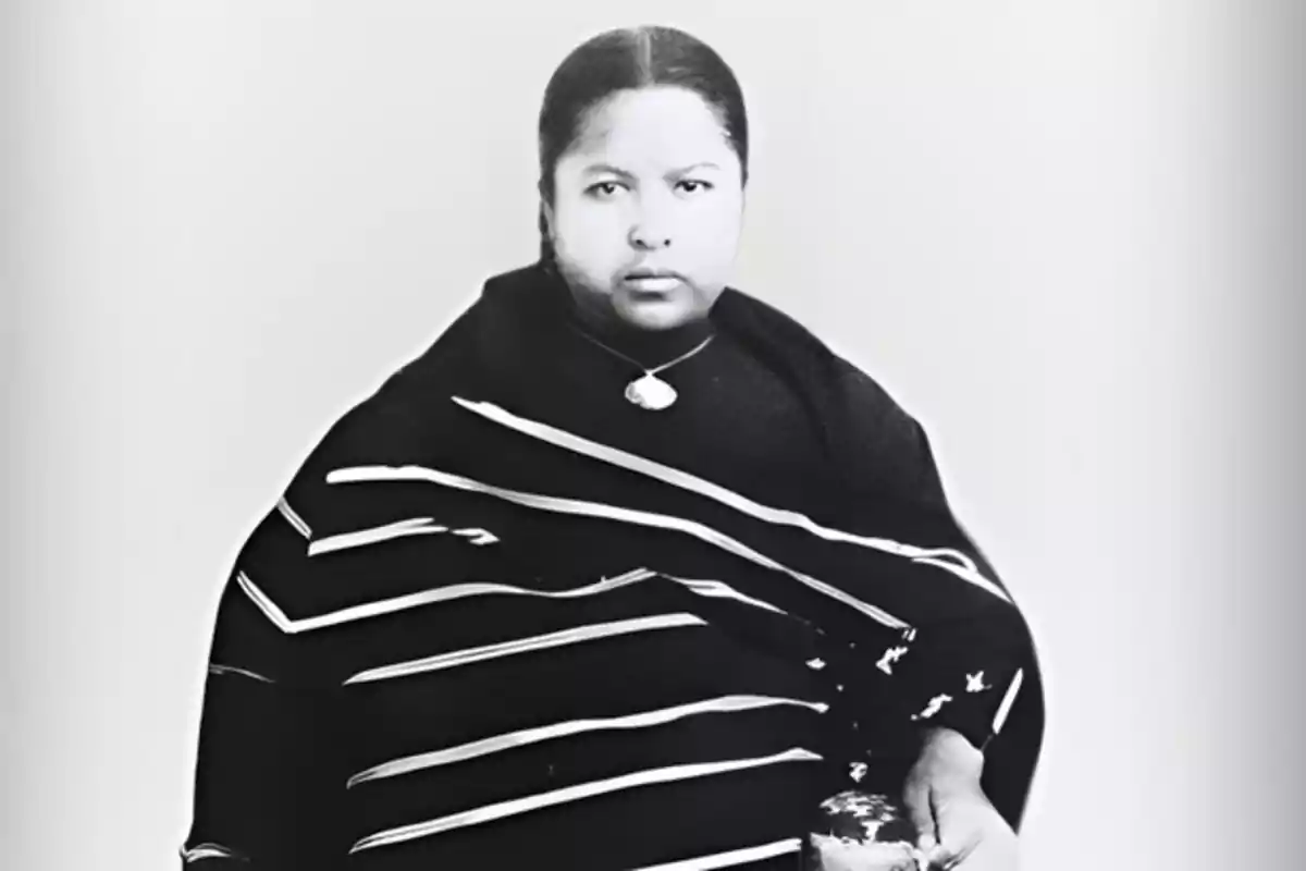 Mujer indígena con cabello recogido, vestida con un rebozo oscuro de rayas claras y un collar, mirando de frente a la cámara Mujer indígena con cabello recogido, vestida con un rebozo oscuro de rayas claras y un collar, mirando de frente a la cámara