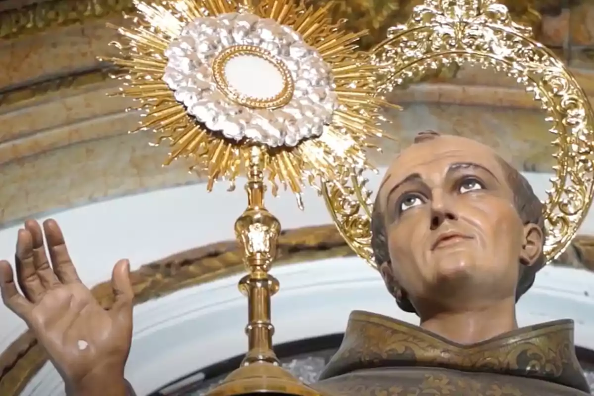 Escultura religiosa d’un sant amb aureola daurada sostenint una custòdia brillant dins d’una església Escultura religiosa d’un sant amb aureola daurada sostenint una custòdia brillant dins d’una església
