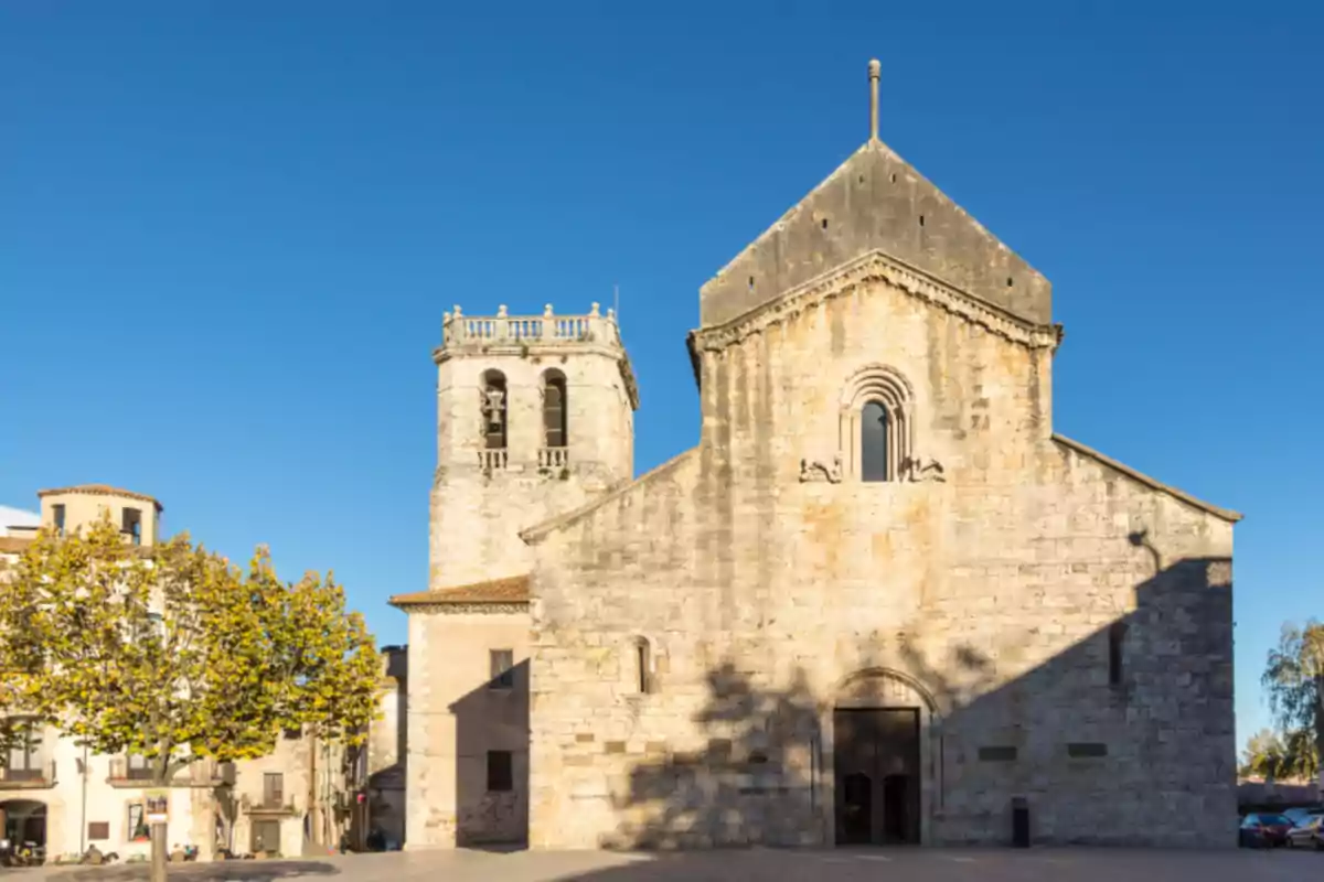 Façana d’una església romànica de pedra amb un campanar a l’esquerra sota un cel blau serè Façana d’una església romànica de pedra amb un campanar a l’esquerra sota un cel blau serè