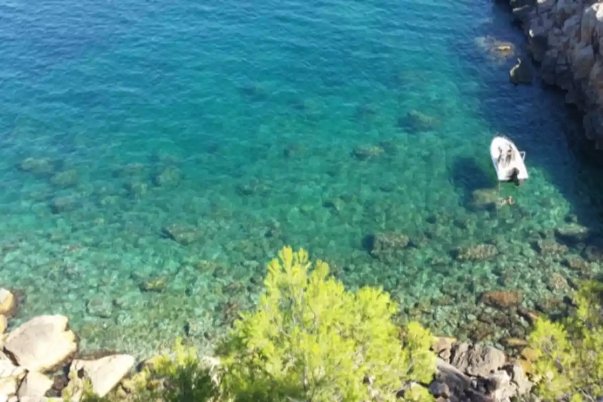 Vista aèria d’una cala rocosa amb aigua turquesa i una petita barca amarrada a prop de la vora Vista aèria d’una cala rocosa amb aigua turquesa i una petita barca amarrada a prop de la vora