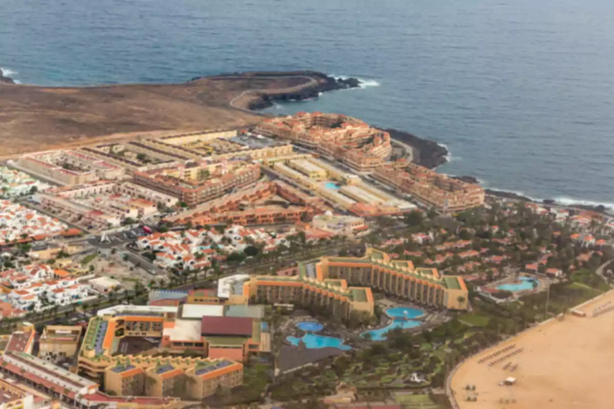 Vista aérea de un complejo turístico junto al mar con piscinas, edificios y una playa amplia Vista aérea de un complejo turístico junto al mar con piscinas, edificios y una playa amplia