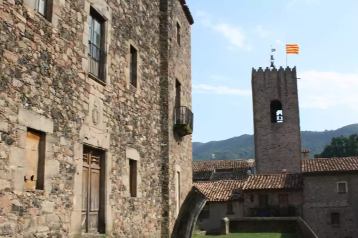 Edifici de pedra antic amb una torre de campanar i una bandera onejant a la part superior, envoltat de muntanyes i cel serè Edifici de pedra antic amb una torre de campanar i una bandera onejant a la part superior, envoltat de muntanyes i cel serè
