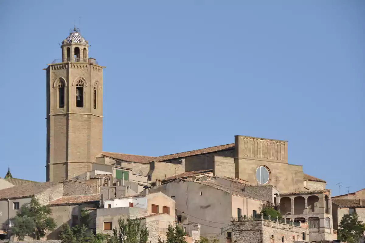 Iglesia de piedra con torre campanario y casas antiguas en primer plano bajo un cielo despejado Iglesia de piedra con torre campanario y casas antiguas en primer plano bajo un cielo despejado